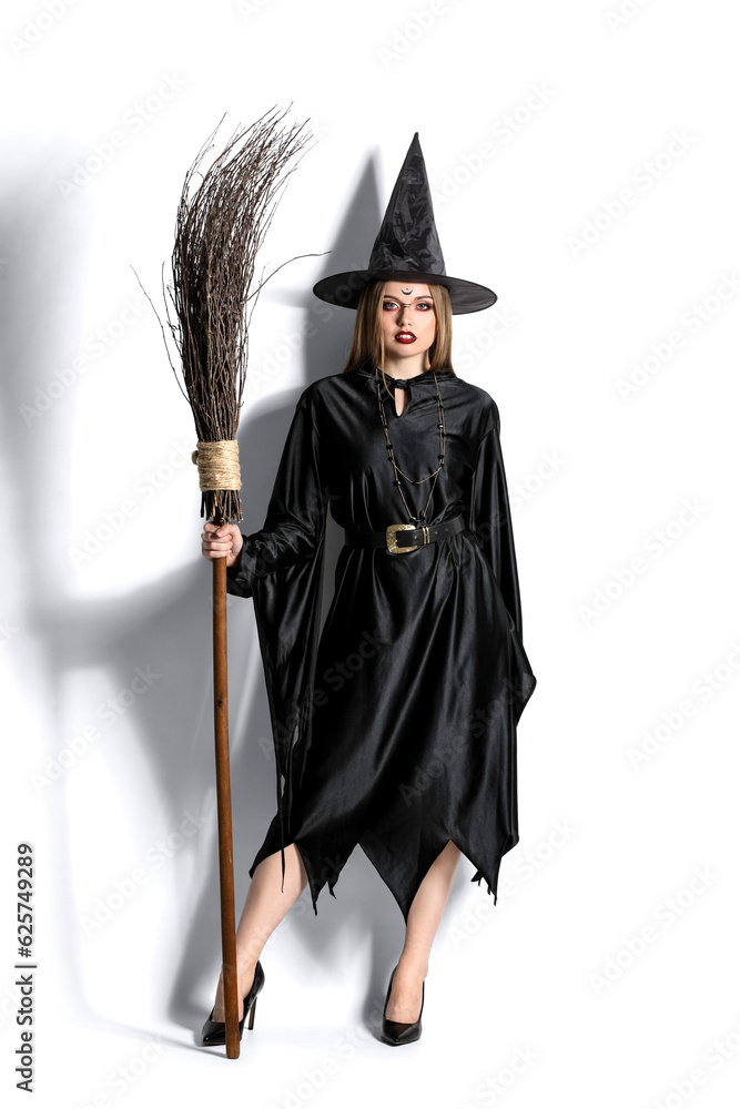Beautiful young witch with broom on white background