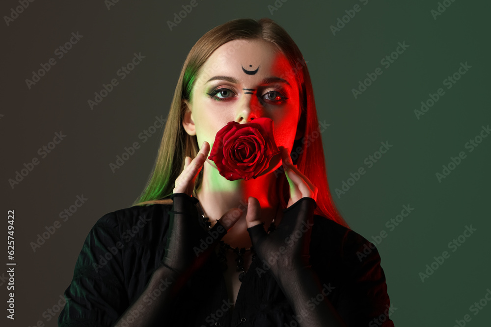 Beautiful young witch with flower on dark background