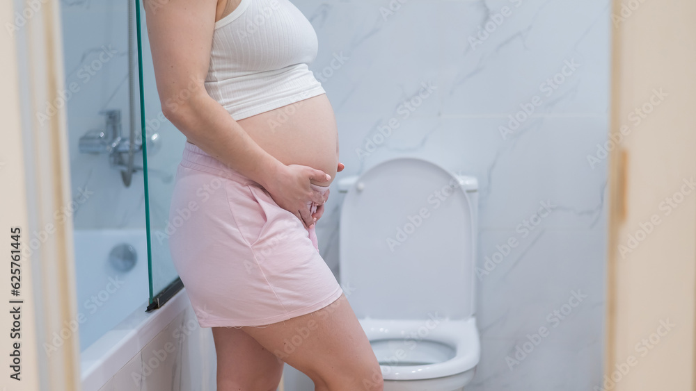 Pregnant woman holding her belly in the toilet. incontinence during ...