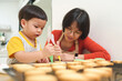 Asian Chinese Mother and her Little boy decorating homemade cookies with icing in kitchen. cooking.