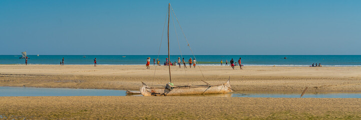coastline from morondava with a baobab wood boat at low tide on sand, background with people panoram