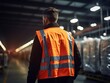 A factory worker man wearing an orange work vest, standing back view in a factory. Generative ai