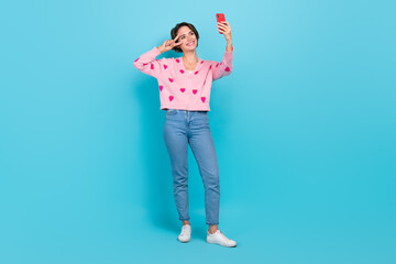 Sticker - Full size length body photo of young friendly woman blogger make video recording show v sign peace selfie isolated on blue color background