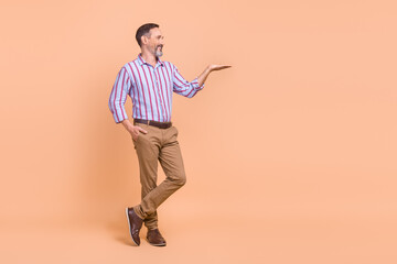 Poster - Full size photo of satisfied cheerful man wear striped shirt look at palm demonstrate offer empty space isolated on beige color background