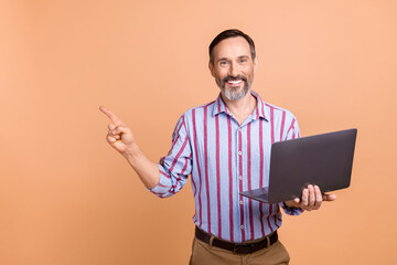 Portrait of handsome successful person hold wireless netbook indicate finger empty space isolated on beige color background