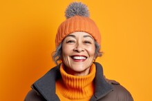 Portrait Of A Smiling Senior Woman In Winter Hat And Coat On Yellow Background