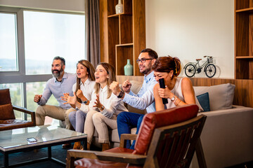 A Team of 3 female and 2 male employees, cheering for their favorite sports team after work