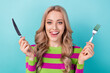 Photo of satisfied woman with curly hairstyle dressed striped sweatshirt holding cutlery lick lips isolated on teal color background