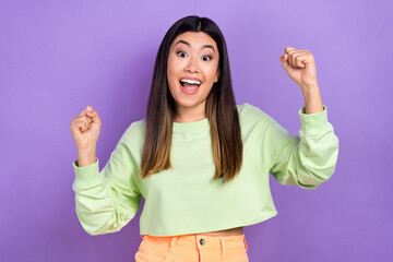 Wall Mural - Photo of cute lucky girl dressed green sweatshirt rising fists yelling isolated violet color background