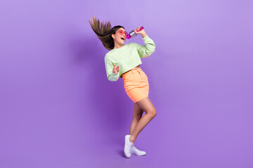 Wall Mural - Full size photo of satisfied cute woman dressed green shirt stylish skirt sing pop song in microphone isolated on purple color background