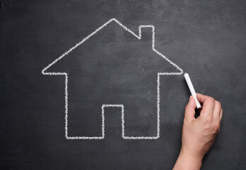 A female hand drawn with chalk on a blackboard a miniature house, concept of rent, mortgage