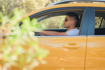 Latino man drives yellow car down a road