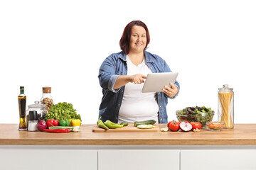 Canvas Print - Young corpulent woman holding a digital tablet behind a kitchen counter with food