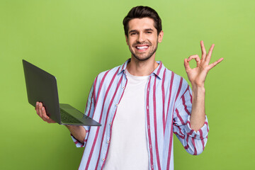 Wall Mural - Portrait of cheerful positive person with brunet hair wear stylish clothes hold laptop show okey isolated on green color background