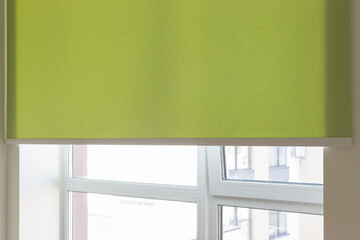 Wall Mural - Details of green fabric roller blinds. Automatic curtain close-up on the window. Selective focus. Motorized shades. City outside the window.