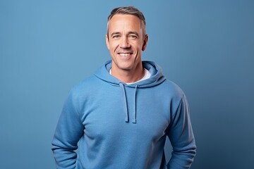 Wall Mural - Portrait of handsome mature man smiling at camera while standing against blue background