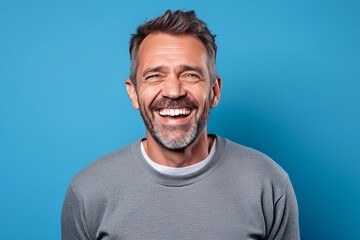 Wall Mural - Portrait of happy mature man laughing and looking at camera on blue background