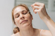 Close-up of a woman applying drops of serum to her face. Summer skin care.