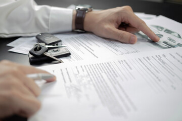 Man signing car insurance document or lease paper. Writing signature on contract or agreement. Buying or selling new or used vehicle. Car keys on wooden table. Warranty or guarantee.