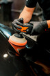 Close-up of a car wash worker using a polishing machine to polish the hood of a black luxury car 