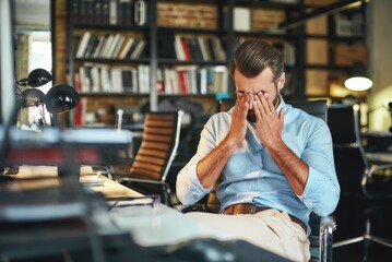 Wall Mural - Hard work. Young exhausted bearded businessman covering his eyes and feeling stressed while sitting in modern office