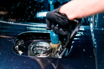 Close-up of a car wash employee washing the fuel cap space of a luxury blue car using a brush 