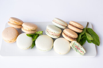 Macaroons of different colors with sprigs of mint on a white background.