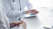 © rogerphoto - Doctor and patient sitting at the table in clinic while using tablet computer. The focus is on female patient's hands, close up. Medicine concept
