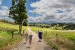 Three people are walking down a stony, dry path in beautiful countryside. This was taken in New Zealand. 