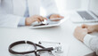 © rogerphoto - Stethoscope lying on the tablet computer in front of a doctor and patient sitting opposite each other and using tablet computer at the background . Medicine, healthcare concept