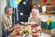 © luckybusiness - Beautiful joyful senior couple with birthday hats sitting at kitchen table together celebrating senior womans birthday.