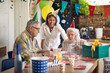 © luckybusiness - Grandma Blows Out Candles Surrounded by Grandpa and Caregivers Amidst Falling Confetti