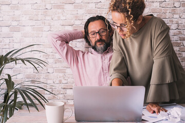 Wall Mural - Two colleagues man and woman working together with computer at office. Small business people lifestyle concept. Entrepreneur and explanation. Mature freelance male stretching arms and female working