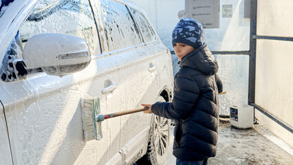 Wall Mural - Little boy washing family car with brush and foam outside at carwash. Concept of parenting, children helping parents and automobile care.