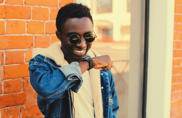 Wall Mural - Portrait of stylish happy smiling african man with smart watch using voice command recorder or takes calling on city street