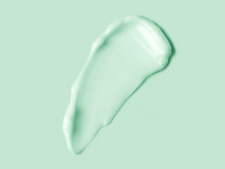 Green cream smear over light green background. Cosmetic hydration cream smudge of liquid reach face or body cream, balm mask texture, top view. Skin care, facial cream, lotion. Herbal cosmetics