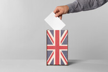 Man Putting His Vote Into Ballot Box Decorated With Flag Of United Kingdom Against Light Background, Closeup