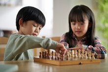Two Cute Asian Children Brother And Sister Playing Chess At Home