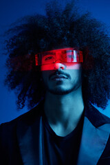 Wall Mural - Fashion portrait of a man with curly hair on a blue background wearing red sunglasses, multinational, colored light, trendy, modern concept.