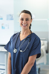 Wall Mural - Portrait of happy caucasian female doctor wearing blue scrubs and stethoscope at hospital