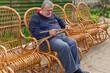 Senior Ukrainian man sorting withe while making whicker rocking chair in summer garden