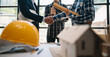 © laddawan - Engineer desk with object paper and tablet with blurry engineer teamwork hardworking to consults about their building project.
