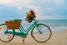 A Vintage Bicycle Leaning Against Sea At Beach In Morning, Wicker Basket With Artificial Flowers On The Bike