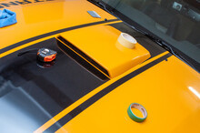 Installation (gluing, Applying) Of Black Strips Decal Of Glossy Foil On A Yellow Classic Sports Car In A Garage.