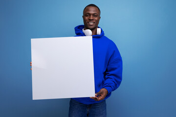Wall Mural - 25 year old young american man shows a paper poster with a mockup for advertising on the background with copy space