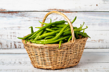 Fresh green pepper in a wicker basket over wooden background. Green chili pepper harvest season concept. Vegetables for a healthy diet