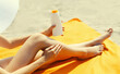 Summer vacation, close up of woman sunbathing and applying suntan cream on her legs lying on sand on the beach