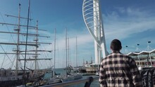 Tourist Man Walk On Pier Of Portsmouth Harbor Entrance With Surrounding Buildings, Spinnaker Tower And Ferries, Slow Motion
