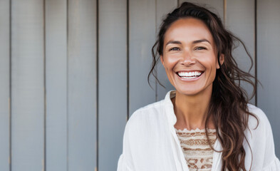 Smiling happy 40 year old brunette woman with long hair isolated against a grey wooden wall.