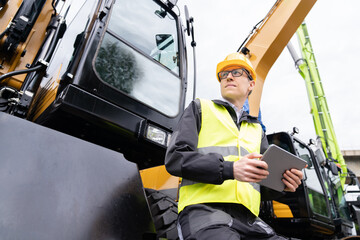 Aufkleber - Engineer in a helmet with a digital tablet next to construction excavators
